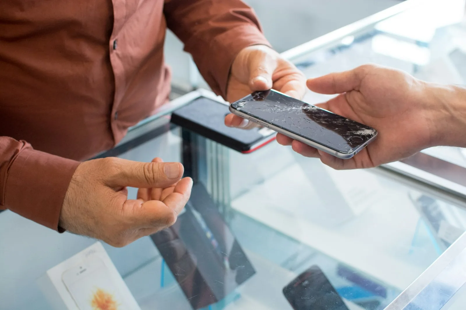 A customer handing a phone across the glass counter